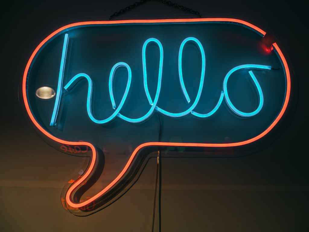 neon sign saying hello in blue within a red neon speech bubble, backdrop is brown